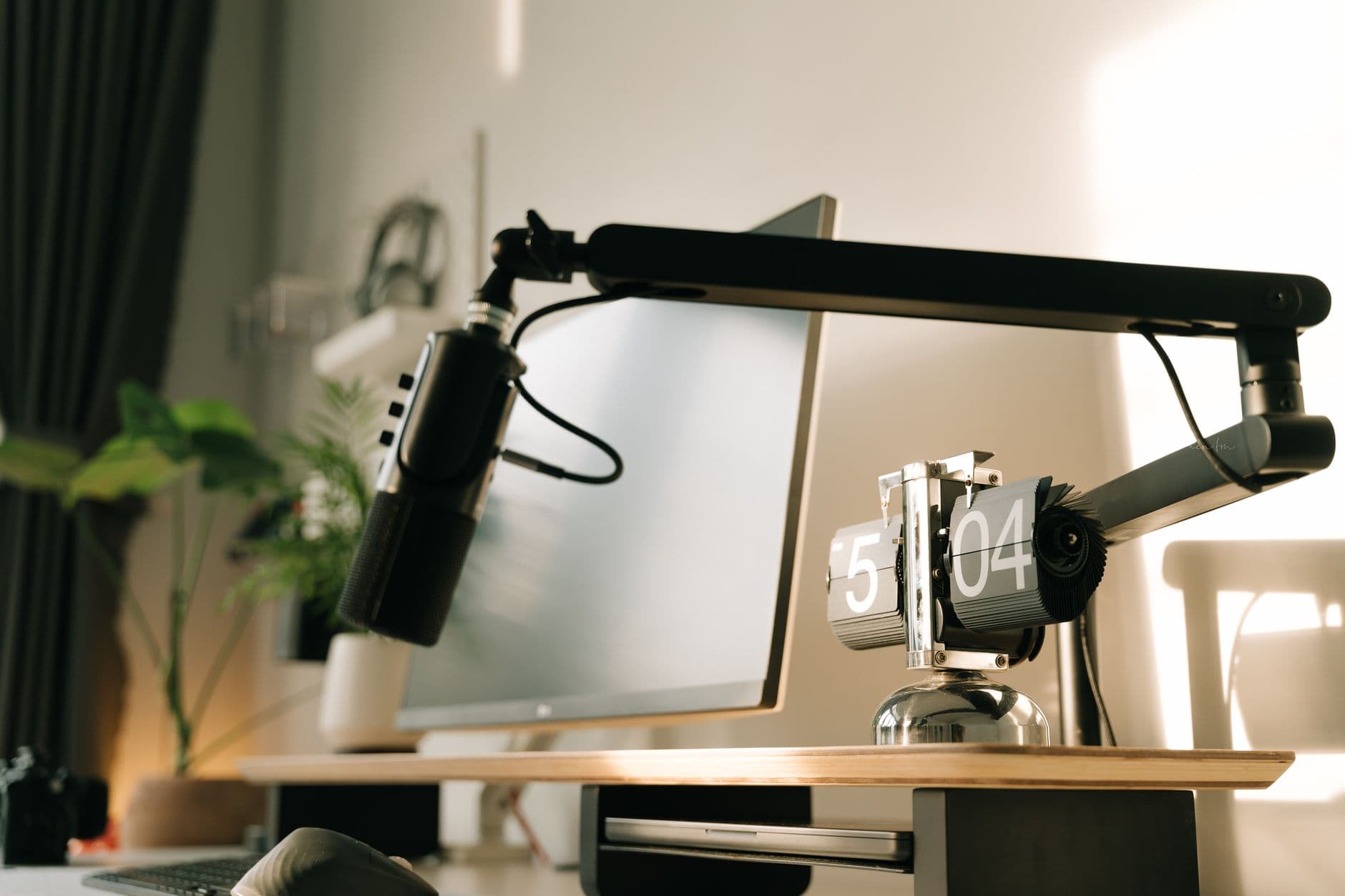 Faceless YouTube creator's desk with monitor, microphone, and flip clock for content planning.