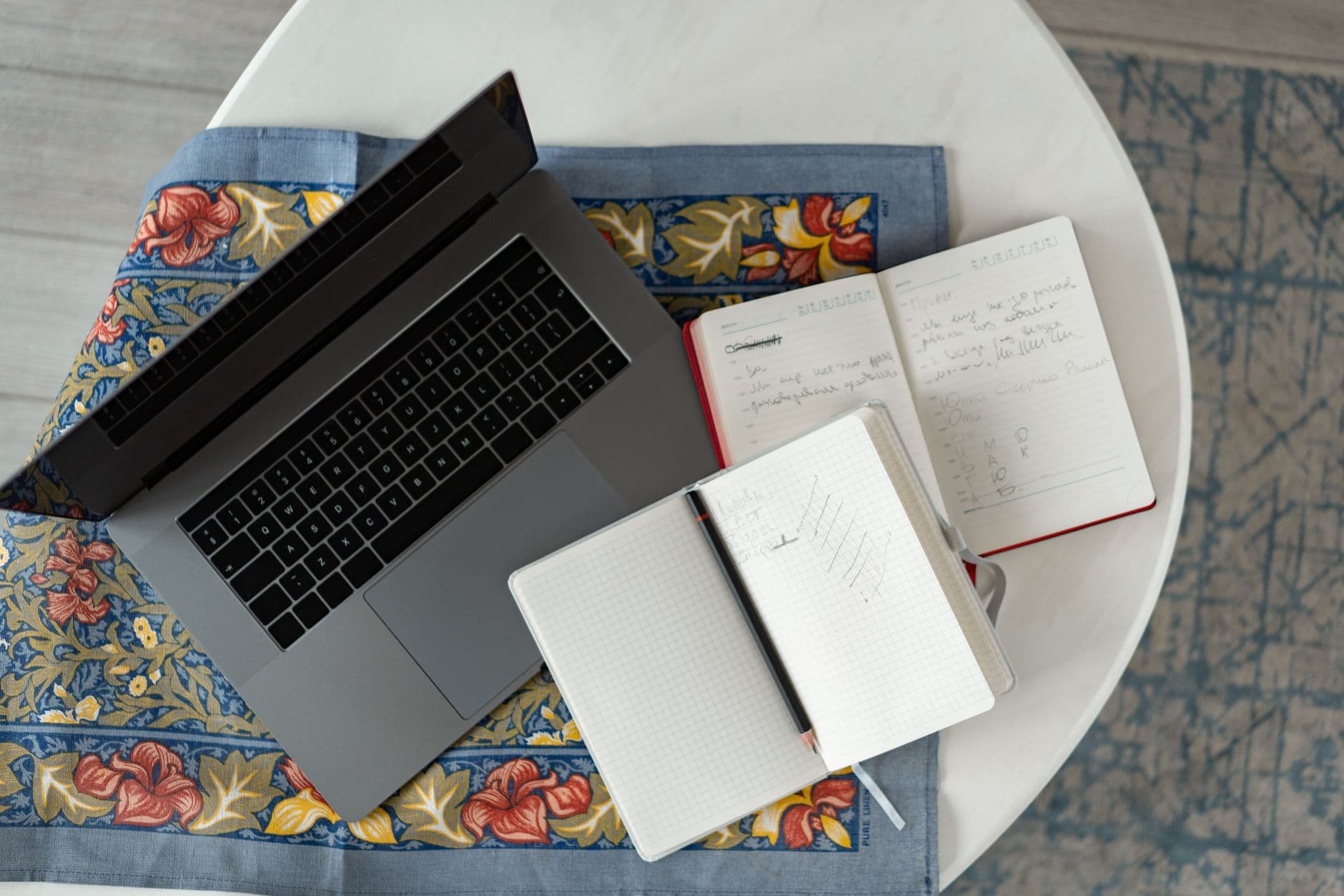 Faceless YouTube creator's workspace with laptop, notebooks, and pen for content planning.