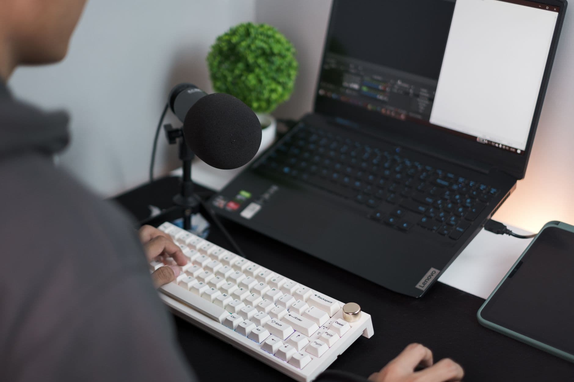 Faceless creator's hands typing on a keyboard next to a laptop displaying video editing software.