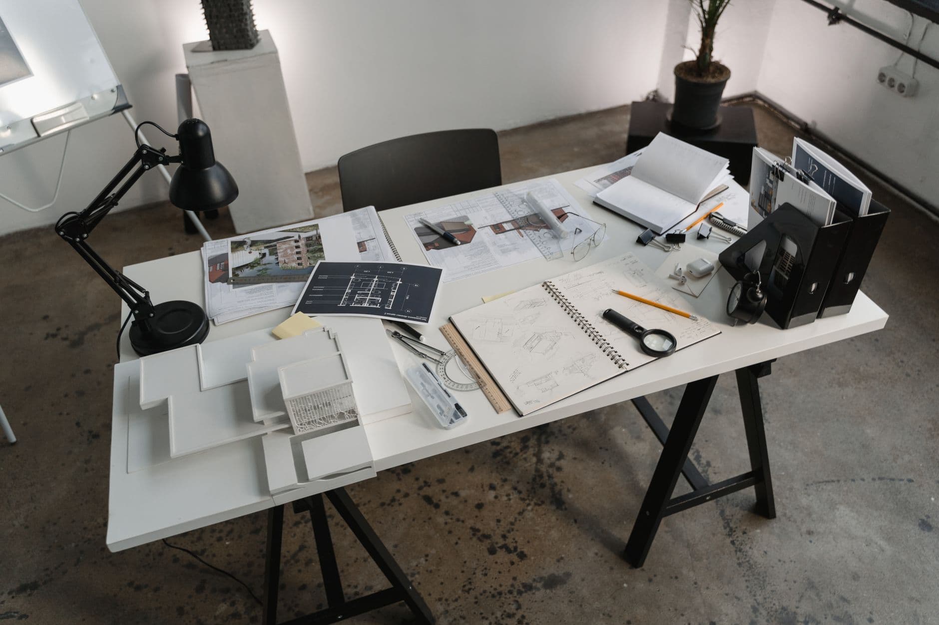 Faceless YouTube creator's desk with blueprints, notebooks, and magnifying glass for niche research.