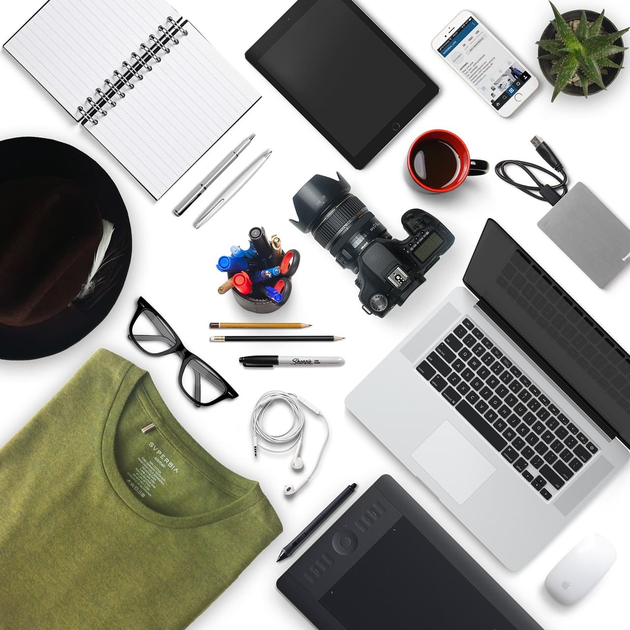 Flat lay of creator tools including laptop, camera, tablet, and notebook for faceless YouTube channel strategy.