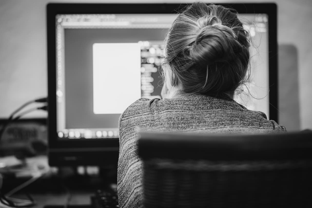 Back of head of a faceless creator at a computer, working on a video editing timeline.