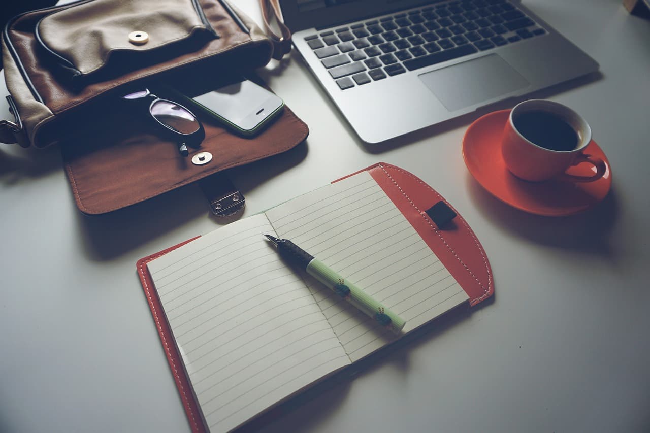 Faceless YouTube creator's desk with laptop, notebook, and coffee for content planning.