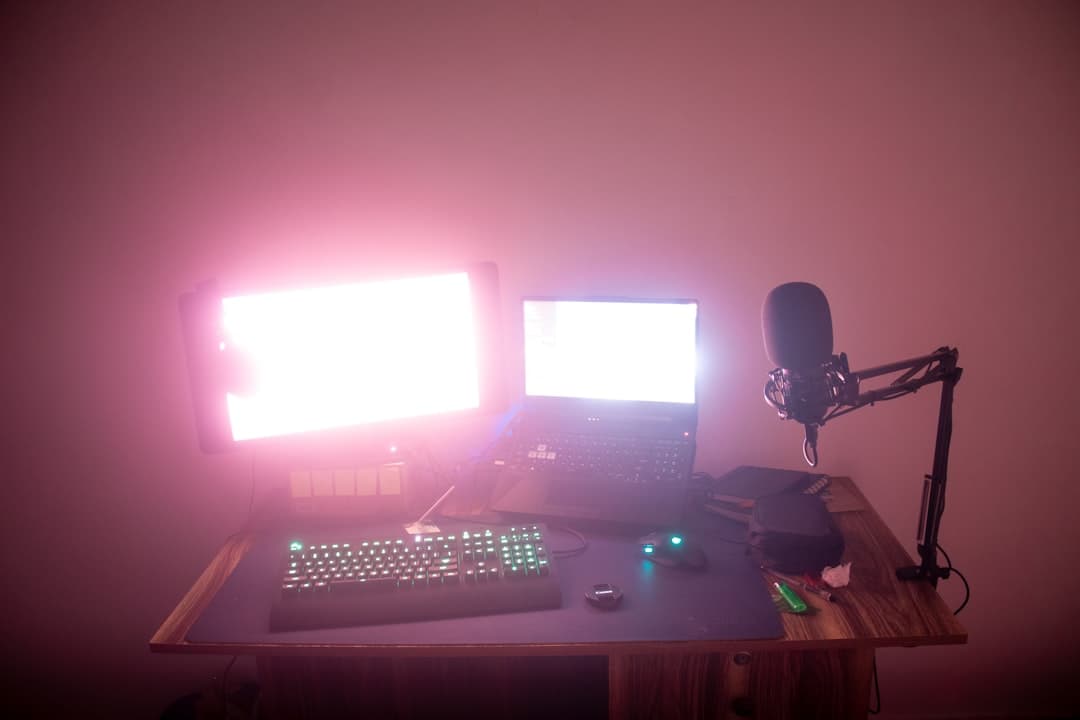 Faceless YouTube creator's desk with dual monitors, laptop, and microphone for narrative engine building.