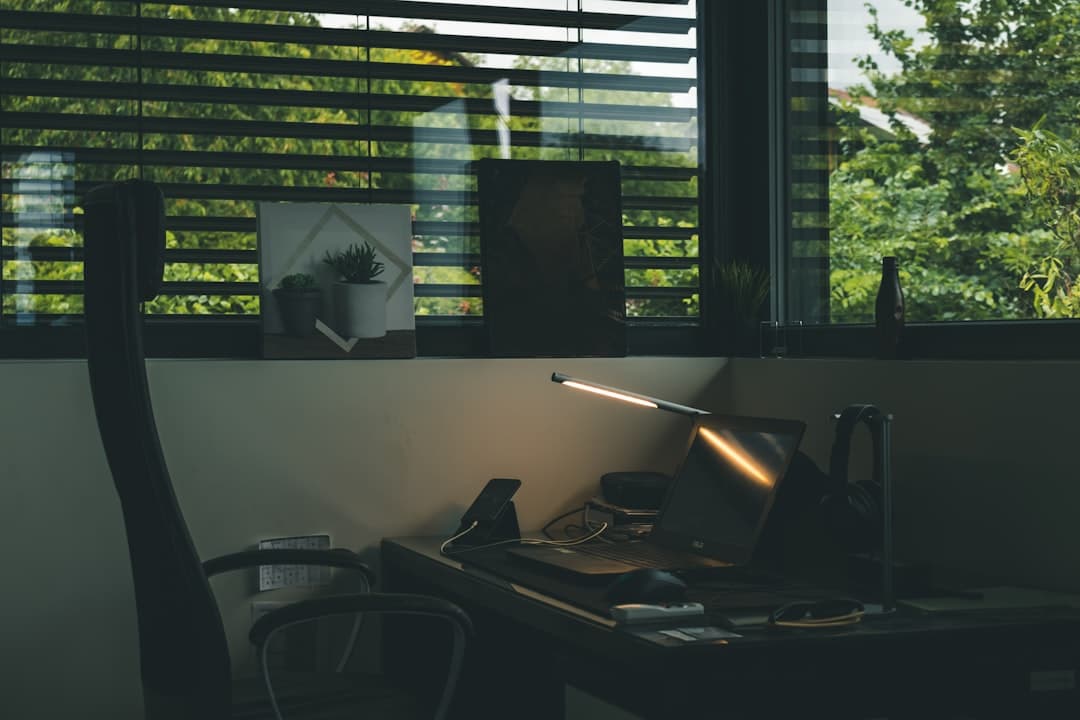Faceless YouTube creator's desk with laptop, lamp, and blinds, suggesting a workspace for content creation.