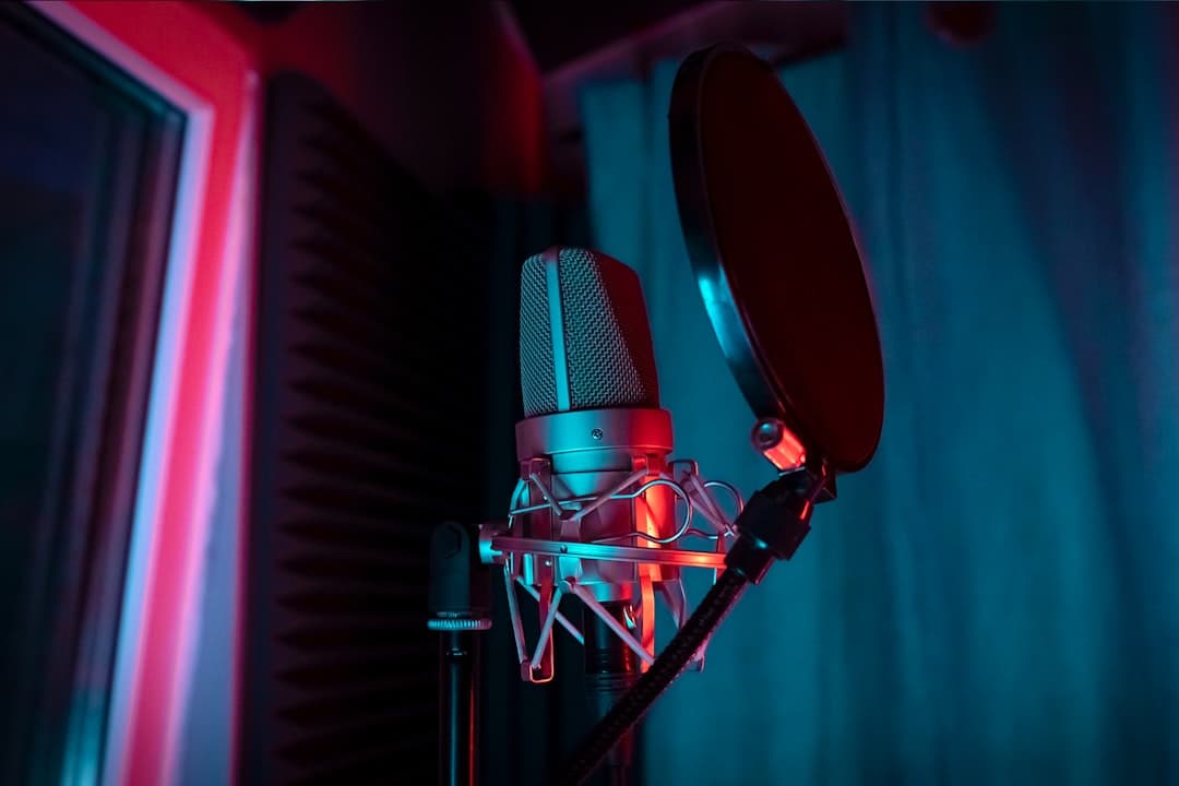 Microphone and pop filter in a dimly lit recording studio with red and blue lighting.