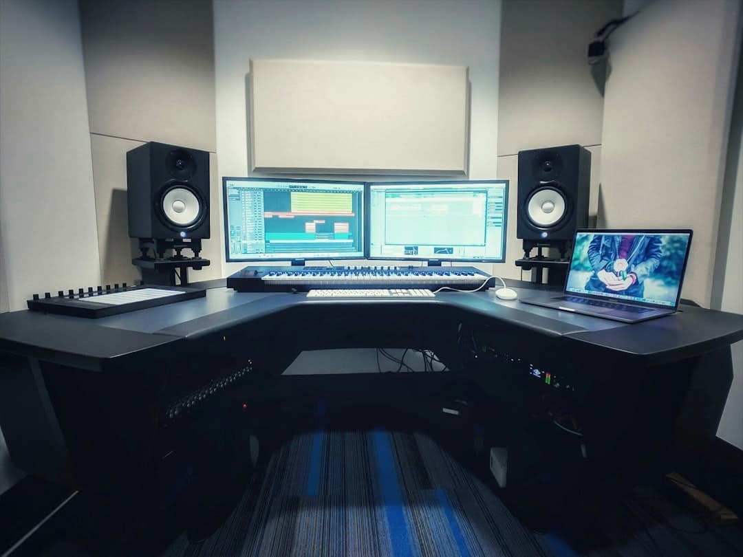 Faceless YouTube creator's audio production desk with dual monitors showing editing software.
