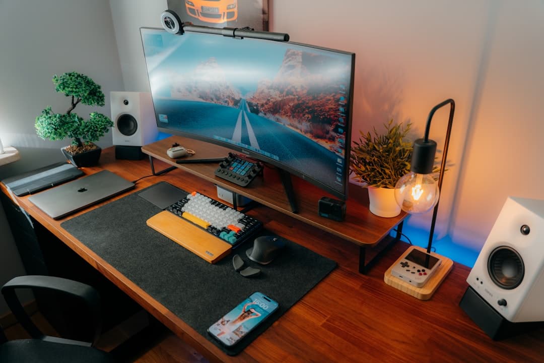 Clean desk setup with curved monitor displaying a road, keyboard, and speakers for content creation.