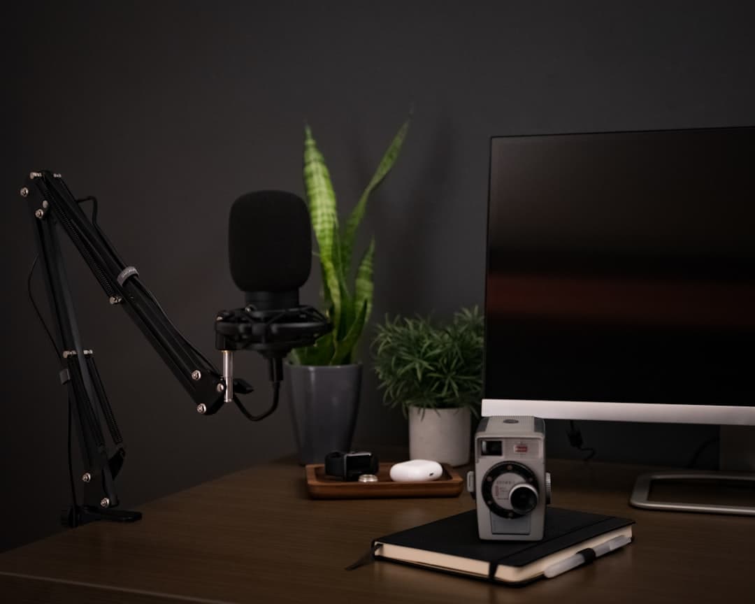 Faceless YouTube creator's desk setup with microphone, computer monitor, and camera for content production.