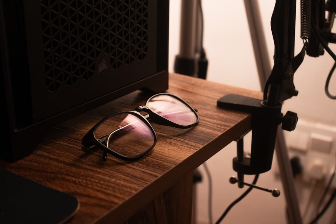 Faceless YouTube creator's desk setup with glasses, computer, and microphone equipment.