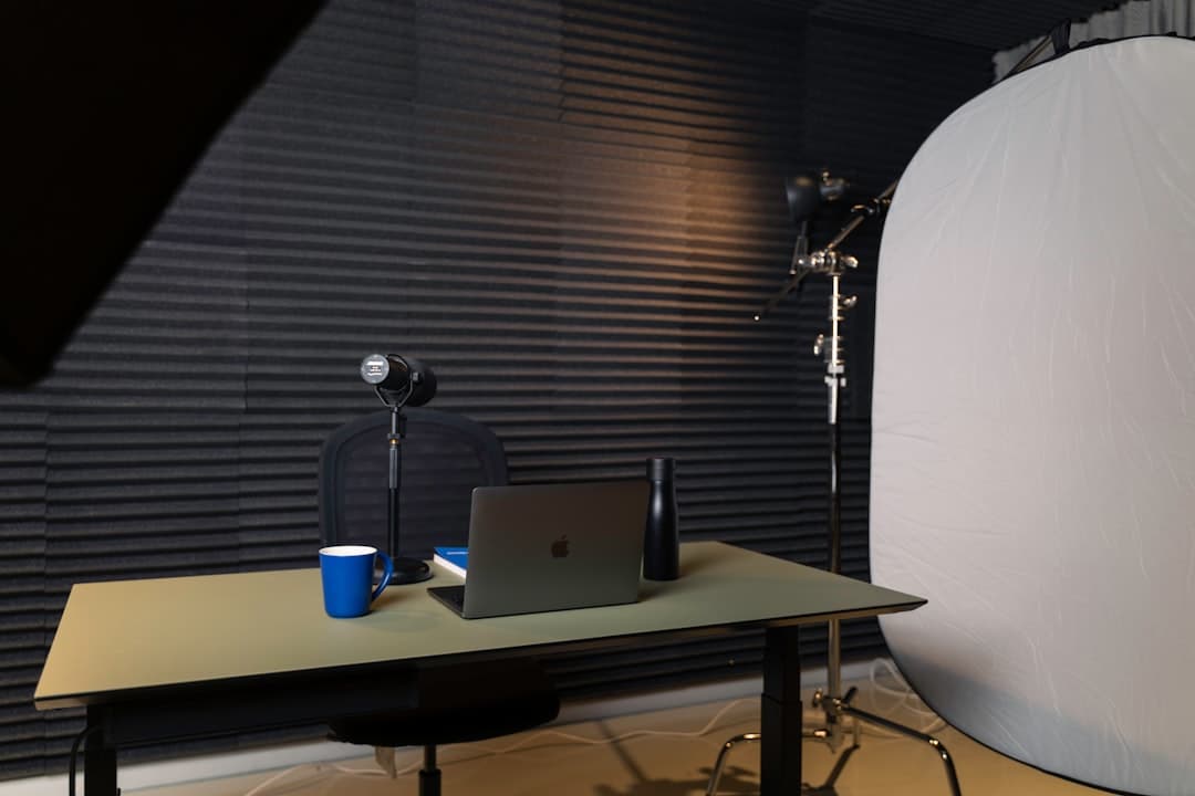 Faceless YouTube creator's empty studio desk with laptop, microphone, and lighting setup.