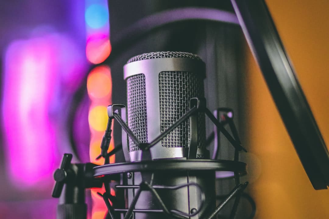 Close-up of a silver studio microphone on a stand, with colorful bokeh lights in the background.
