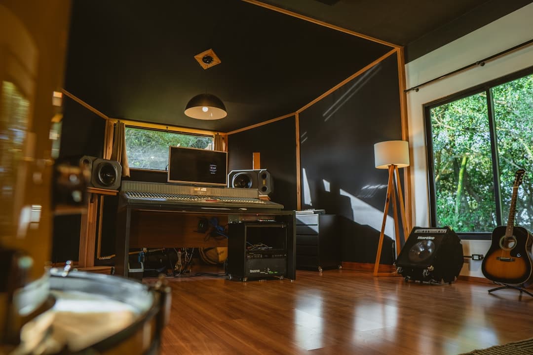 Faceless YouTube creator's studio with monitors, mixing board, and guitars for content production.