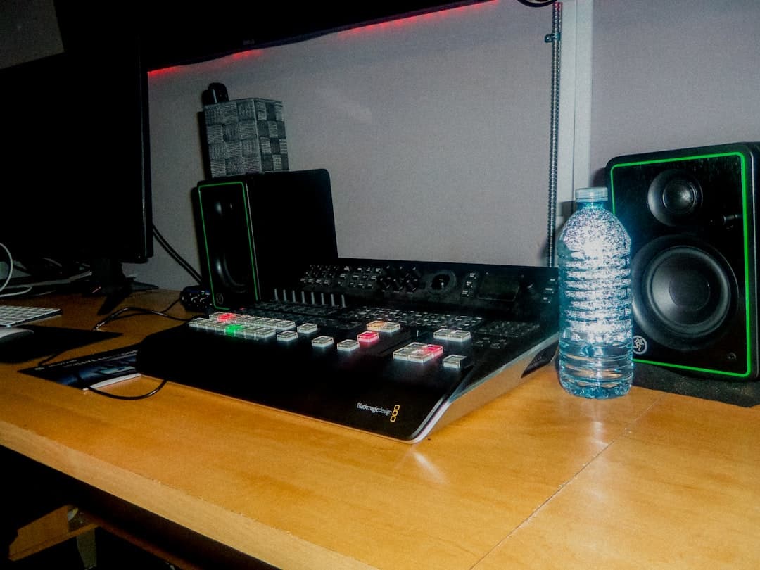 Desk with audio production equipment, including a mixer, speakers, and a water bottle.