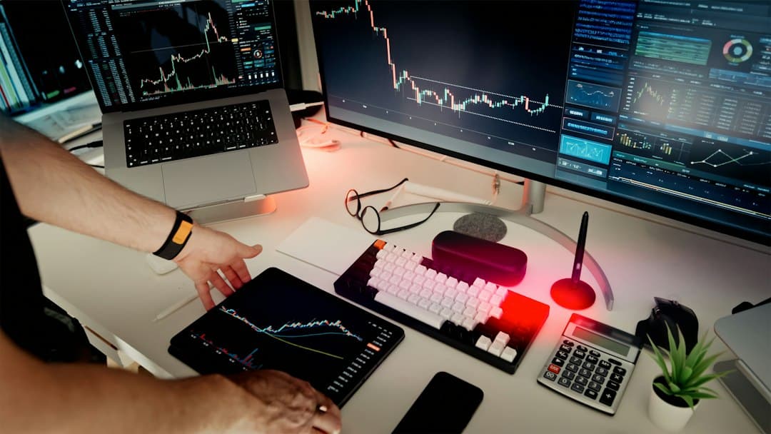 Faceless YouTube creator's desk with multiple monitors showing analytics and trading charts.