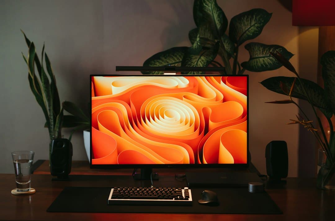 Clean desk setup with a monitor displaying abstract art, keyboard, mouse, and plants.